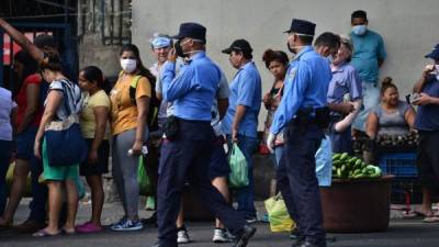 Police agents walk past people making a line to buy groceries at a street market in Tegucigalpa, on March 22, 2020, in spite of the curfew imposed by the government against the spread of the new coronavirus. - Authorities have confirmed 26 cases of COVID-19 in the country so far. (Photo by ORLANDO SIERRA / AFP)