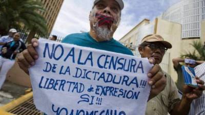 Un hombre con un bozal y un cartel participa de un plantón frente a la Asamblea Nacional (AN) en rechazo a la iniciativa de Ley. EFE