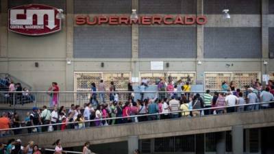 People queue outside a supermarket in Caracas to buy basic foodstuffs and household products on November 10, 2017.In crisis-stricken Venezuela, the cost of the basic basket of goods soared to nearly 2.7 million bolivars in September, the equivalent of six minimum monthly wages. / AFP PHOTO / FEDERICO PARRA