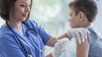 A nurse is giving a elementary age boy a flu shot at the doctor's office.