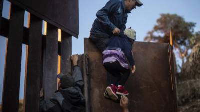 Central American migrants who have been travelling in a caravan hoping to get to the United States, climb the metal barrier separating Mexico and the US to cross from Playas de Tijuana in Mexico into the United States, on December 2, 2018. - Thousands of Central American migrants, mostly Hondurans, have trekked for over a month in the hopes of reaching the United States. (Photo by Pedro PARDO / AFP)