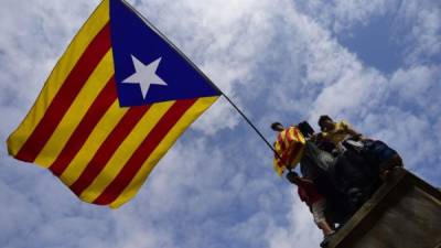 Un grupo de jóvenes sostiene una bandera de Cataluña sobre uno de los monumentos de la ciudad de Barcelona.