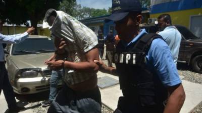 Uno de los detenidos se cubre el rostro mientra es escoltado por un custodio.