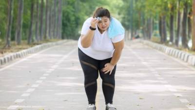 Picture of overweight woman looks tired after jogging on the road while wiping her sweat