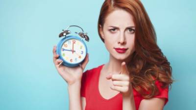 Redhead girl with alarm clock on blue background.