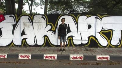 El artista urbano Robowobo posa en el este de Yakarta frente a un grafiti con el texto 'Reclaim Jakarta', que hace referencia al proyecto ideado por Isrol Triono, en el que también han participado, además de estos dos, los grafiteros Aryo Dewa Bharata, Wacky y Nur Nus. EFE