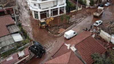 Con la ayuda de maquinaria, los residentes de la localidad de Mandra tratan de despejar sus enlodadas calles.