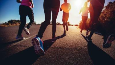 Unusual low angle back view of a group of friends jogging outdoors on a summer afternoon with sun flare