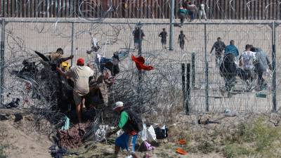 Migrantes cruzan una alambrada de navajas y púas, en la frontera que divide a México de los Estados Unidos, el 14 de marzo de 2024, en Ciudad Juárez (México).