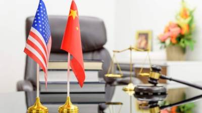 Flag of US USA and China put together on a table with books, gavel and a balance of justice behind. A symbol of cooperation between Washington & Beijing i.e. military dialogue, diplomatic negotiation. (Flag of US USA and China put together on a table