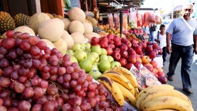 Transeúntes pasan frente a un puesto de frutas y verduras en un mercado sampedrano. FOTO: Franklyn Muñoz