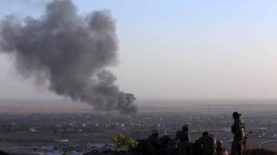 Iraqi Kurdish Peshmerga fighters look on as smoke billows from the town Makhmur, about 280 kilometres (175 miles) north of the capital Baghdad, during clashes with Islamic State (IS) militants on August 9, 2014. Makhmur, is one of the areas that had been attacked by jihadist fighters in recent days. AFP PHOTO/SAFIN HAMED