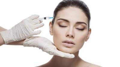 Beautiful young woman gets beauty injection in forehead from sergeant. Isolated over white background.