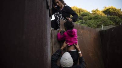 Migrantes centroamericanos de la caravana escalan la barrera de metal que separa a México y EEUU. Foto: AFP