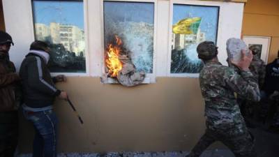 Members the Hashed al-Shaabi, a mostly Shiite network of local armed groups trained and armed by powerful neighbour Iran, smash the bullet-proof glass of the US embassy's windows in Baghdad with blocks of cement after breaching the outer wall of the diplomatic mission on December 31, 2019 to vent their anger over weekend air strikes that killed pro-Iran fighters in western Iraq. - It was the first time in years protesters have been able to reach the US embassy in the Iraqi capital, which is sheltered behind a series of checkpoints in the high-security Green Zone. (Photo by AHMAD AL-RUBAYE / AFP)