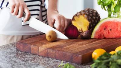 Woman on diet cutting fruits on wooden board in kitchen with glossy countertop. Fruitarian diet concept