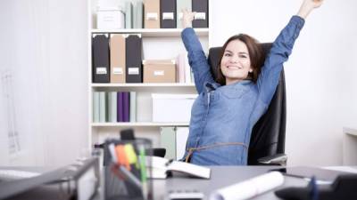 Happy Young Office Woman Sitting on her Chair Stretching her Arms While Looking at the Camera.