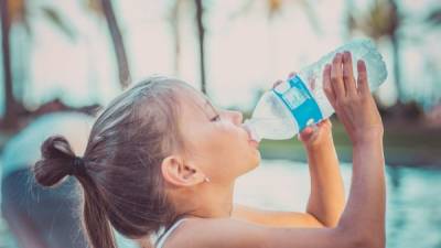 A child is drinking clean water from a bottle. Hot summer day.