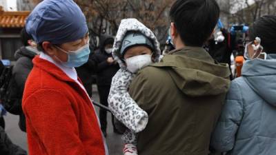 A nurse (L) looks at a one-year-old boy as his father and mother (R) speak to the media during a ceremony marking their release after recovering from the COVID-19 coronavirus, at the Youan Hospital in Beijing on February 14, 2020. - Youan Hospital is one of twenty hospitals in Beijing treating coronavirus patients. Six health workers have died from the COVID-19 coronavirus in China and more than 1,700 have been infected, health officials said on February 14, underscoring the risks doctors and nurses have taken due to shortages of protective gear. (Photo by GREG BAKER / AFP)