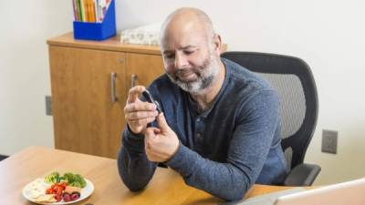 A diabetic man at work testing his blood to monitor his blood glucose levels so he can manage his diabetes.