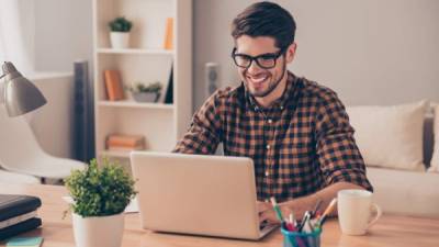 Handsome cheerful young man in glasses typing on laptop