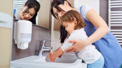 Kid washing hands with mom in the bathroom.