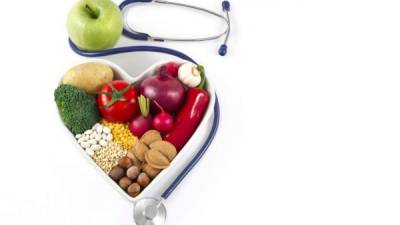 Heart health, and cholesterol diet concept. Healthy foods in heart shaped bowl with stethoscope and green apple on white background.