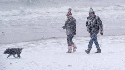 A couple walk their dog on the beach as heavy snow falls in the sea side resort of Scarborough in North Yorkshire on February 27, 2018. A blast of Siberian weather sent temperatures plunging across much of Europe on Tuesday, causing headaches for travellers and leading to several deaths from exposure as snow carpeted palm-lined Mediterranean beaches. / AFP PHOTO / Anthony Devlin