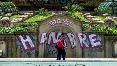 Una pareja camina por graffitis que dice 'We Are Hungry' y 'Maduro Dictator' en Caracas el 8 de agosto de 2017. AFP