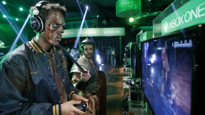 Un hombre disfrazado de zombi juega Dead Rising Three junto a un hombre que representa a un soldado romano del videojuego Ryse: Son of Rome, en la nueva la XBox One.
