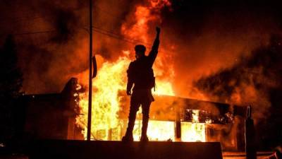 TOPSHOT - A protester reacts standing in front of a burning building set on fire during a demonstration in Minneapolis, Minnesota, on May 29, 2020, over the death of George Floyd, a black man who died after a white policeman kneeled on his neck for several minutes. - Violent protests erupted across the United States late on May 29 over the death of a handcuffed black man in police custody, with murder charges laid against the arresting Minneapolis officer failing to quell seething anger. (Photo by Chandan KHANNA / AFP)