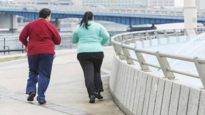 Rear view of an overweight Hispanic woman and a young mixed race Hispanic and Caucasian man running or jogging together outdoors in an urban setting.