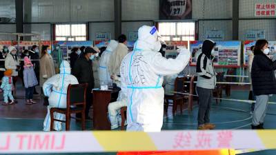 Oficiales en China utilizan trajes de protección para guiar a un grupo de residentes que se realizan test de PCR ante la propagación de la nueva cepa del covid 19 por el mundo.