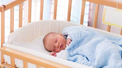 Newborn baby in hospital room. New born child in wooden co-sleeper crib. Infant sleeping in bedside bassinet. Safe co-sleeping in a bed side cot. Little boy taking a nap under knitted blanket.