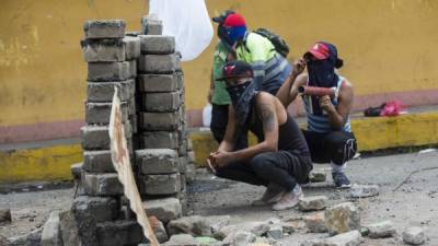 Varios jóvenes se refugian detrás de una barricada de adoquines durante un enfrentamiento con la Policía. EFE