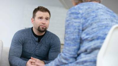 A young husband sits across from his therapist looking defeated. He is upset because he realizes that he has not been as attentive to his wife's needs as he should be.