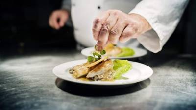 Professional chef putting the final flourish to the dish by adding a sprig of watercress to the dish of slow cooked chicken breast served on a bed of bulgur risotto. Colour, horizontal with some copy space. Photographed in a restaurant on the island of MÃ ̧n in Denmark.