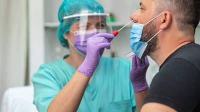 Female healthcare worker wearing protective workwear taking nose swab test from middle aged man in protective face mask, Covid-19 pandemic outbreak