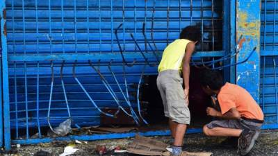 Niños curiosos se asoman pro un agujero creado por saqueadores en un negocio de abarrotes.