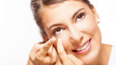 Beautiful young woman putting in her contact lenses, on white background