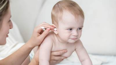 Closeup photo of young mother cleaning baby's ear with cotton swab after bathing