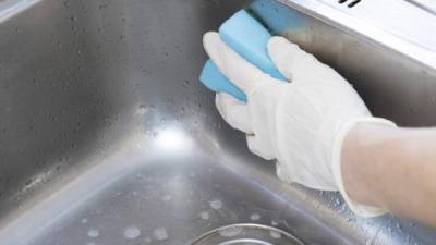 Woman is cleaning the kitchen sink by the sponge.