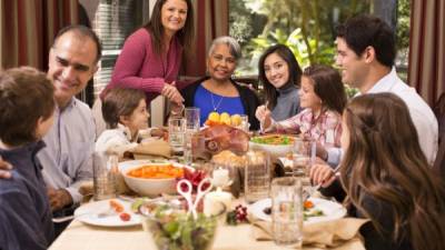 Multi-ethnic, multi-generation family enjoying Thanksgiving or Christmas dinner together around the dining table at grandmother's home. Latin descent, African descent, mixed race, and Caucasian family members. Ham and other food on table.