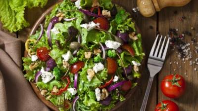 Top view of a colorful spring salad on rustic wood table. The ingredients included in the salad are lettuce, radicchio, spanish onion, black olives, capers, broccoli, bell pepper, walnut and goat cheese. The salad is served on a wood plate and a fork is beside it. A pepper grinder is tilted coming from the upper-right side of the frame and a textile napkin is at the lower-left of the frame. DSRL studio photo taken with Canon EOS 5D Mk II and Canon EF 70-200mm f/2.8L IS II USM Telephoto Zoom Lens