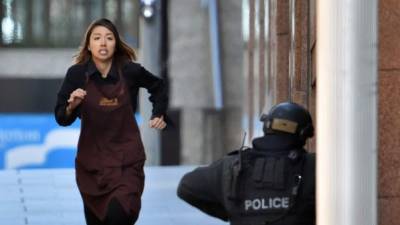 Una empleada abandona la cafetería donde trabaja y que un hombre armado tiene tomada desde primeras horas de la mañana en Sídney (Australia) hoy, lunes 15 de diciembre de 2014. EFE