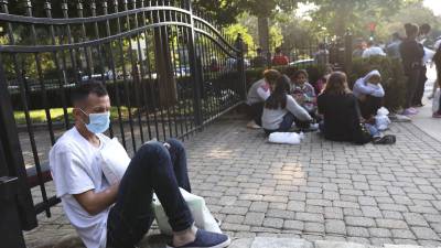 Migrantes venezolanos y mexicanos esperan en las afueras de la residencia de Harris tras ser dejados por un autobús en el que fueron enviados desde Texas.