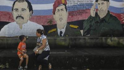 A woman and child sit on a bench in front of a mural depicting Nicaragua's President Daniel Ortega (L), late Venezuela's President Hugo Chavez (C) and former Cuba's President Fidel Castro in Managua on November 4, 2016 head of Sunday's general elections.Ortega looks to be heading for an easy re-election to a fourth term this weekend, with his wife as his running mate. Surveys credit the pair with more than 60 percent voter support for Sunday's balloting, far ahead of their rivals. But critics inside and outside the country are calling foul over tactics that have sidelined the opposition and restricted foreign scrutiny. / AFP PHOTO / INTI OCON
