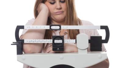 Sad and worried woman on a medical weight scale. white background.