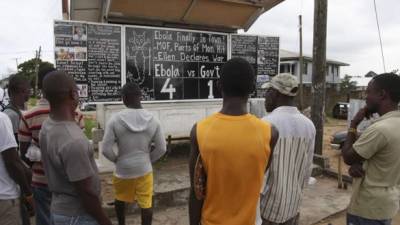 Un grupo de personas observa el tablero que anuncia la cifra de víctimas mortales de Ébola en el país, en una valle de Monrovia (Liberia).