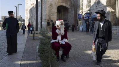 Un judíos ultraortodoxo observa con descontento a un palestino disfrazado de Papá Noel que reparte árboles de Navidad en la Puerta de Jaffa, dentro de la ciudad vieja de Jerusalén (Israel). EFE